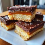 Close-up of stacked homemade Twix bars showing shortbread, caramel, chocolate topping, and sea salt flakes.