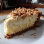A close-up slice of rich Million Dollar Pie showing a graham cracker crust, creamy filling, and crunchy pecan topping.
