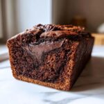 A close-up of a loaf of moist chocolate bread, showing a rich, dark crumb and a melted chocolate swirl inside.