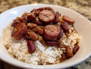 A close-up of a white bowl filled with fluffy white rice topped generously with red kidney beans and sliced smoked sausage, representing amazing 1-Pot beans and rice.