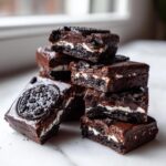 A stack of rich, dark chocolate Oreo fudge squares featuring visible white cream filling and topped with Oreo pieces.