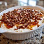 Close-up of creamy pecan pie dip topped with caramel sauce and chopped pecans in a white serving dish.