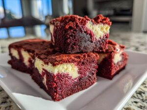 Close-up of stacked, rich red velvet cheesecake brownies showing the vibrant red cake and creamy white cheesecake swirl.