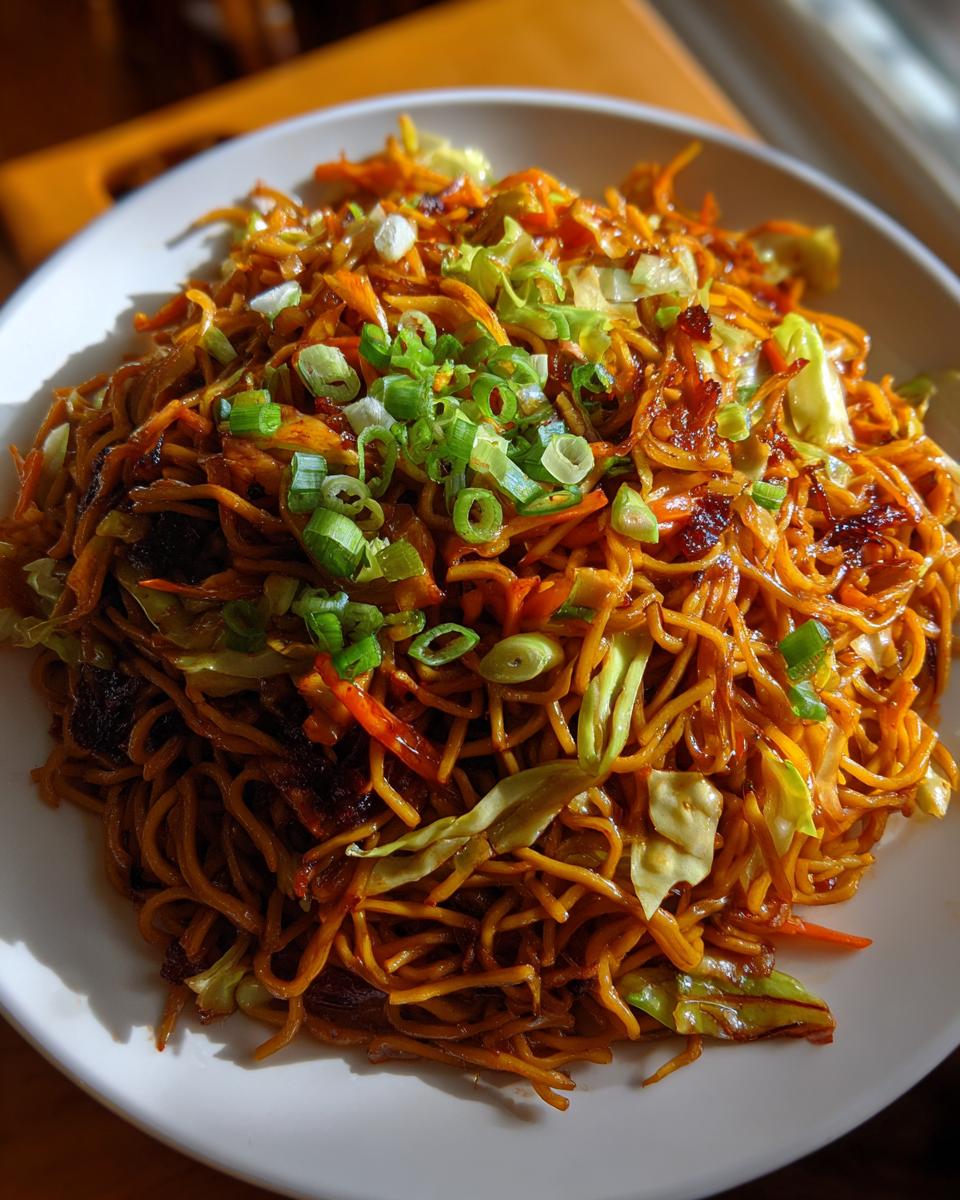 A close-up of a generous serving of savory fried noodles mixed with cabbage and carrots, topped with fresh green onions.