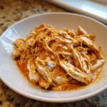 Close-up of shredded chicken coated in a rich, creamy orange sauce, ready to eat, from the crockpot marry me chicken recipe.