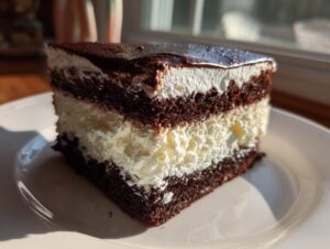 A decadent slice of 3-layer italian love cake featuring dark chocolate cake, white cream filling, and a shiny chocolate glaze.