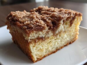 Close-up of a moist slice of sour cream coffee cake featuring a rich cinnamon swirl and thick, sugary crumb topping.