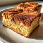 A close-up of a square piece of snickerdoodle blondies with a thick, sugary cinnamon topping on a white plate.
