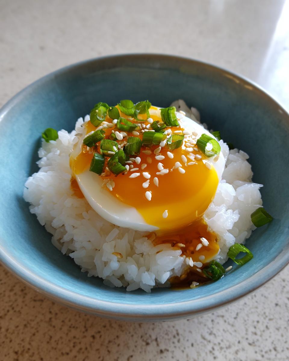 A soft-boiled egg with a runny yolk served over white rice, topped with green onions and sesame seeds, resembling marinated eggs.