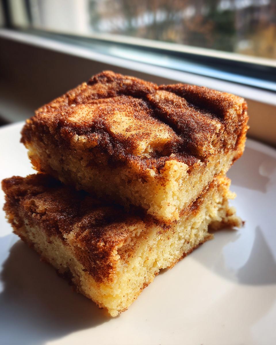 Two stacked squares of soft snickerdoodle blondies topped with a rich cinnamon-sugar swirl, sitting on a white plate.