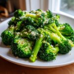 Close-up of bright green steamed broccoli florets topped with grated cheese and seasoning.