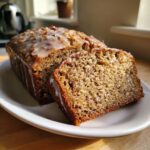 A loaf of sweet Alabama pecan bread, partially sliced, covered in a sweet glaze and chopped pecans.
