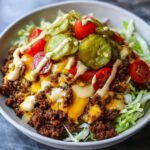 A close-up of a delicious cheeseburger bowl featuring seasoned ground beef, melted cheese, pickles, tomatoes, and a drizzle of sauce over lettuce.