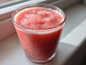 Close-up of a frosty glass filled with a vibrant red watermelon smoothie, condensation visible on the outside.