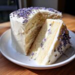 A slice cut from an amazing earl grey lavender cake, revealing layers of cake and white frosting, topped with dried lavender.