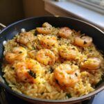 Close-up of perfectly cooked shrimp nestled in creamy shrimp orzo pasta, garnished with fresh herbs in a black skillet.