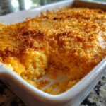 Close-up of a creamy, baked hot crab dip recipe with a golden brown, crispy breadcrumb topping in a white casserole dish.