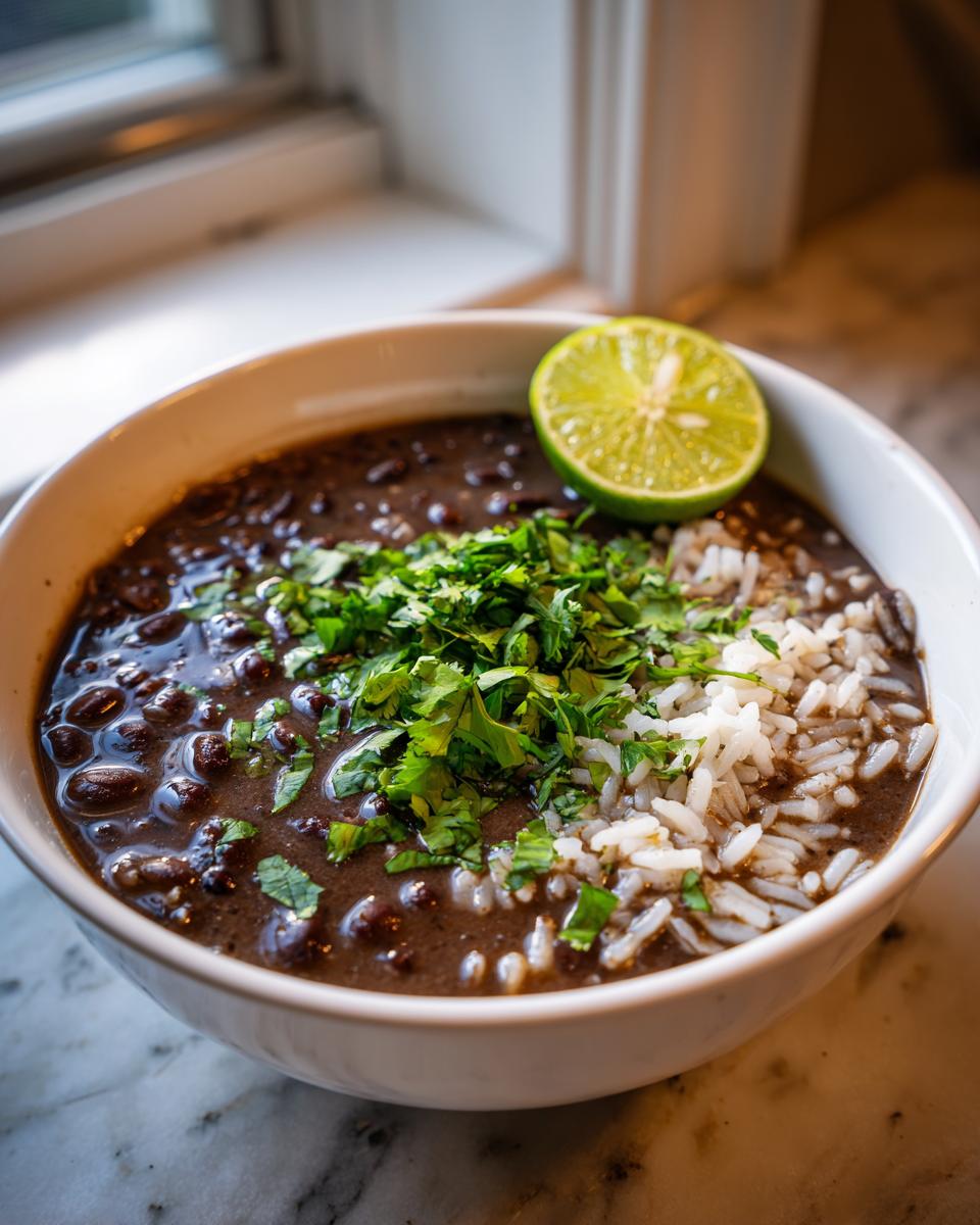 A close-up of a bowl of rich black bean and rice soup topped with fresh cilantro and a lime wedge.