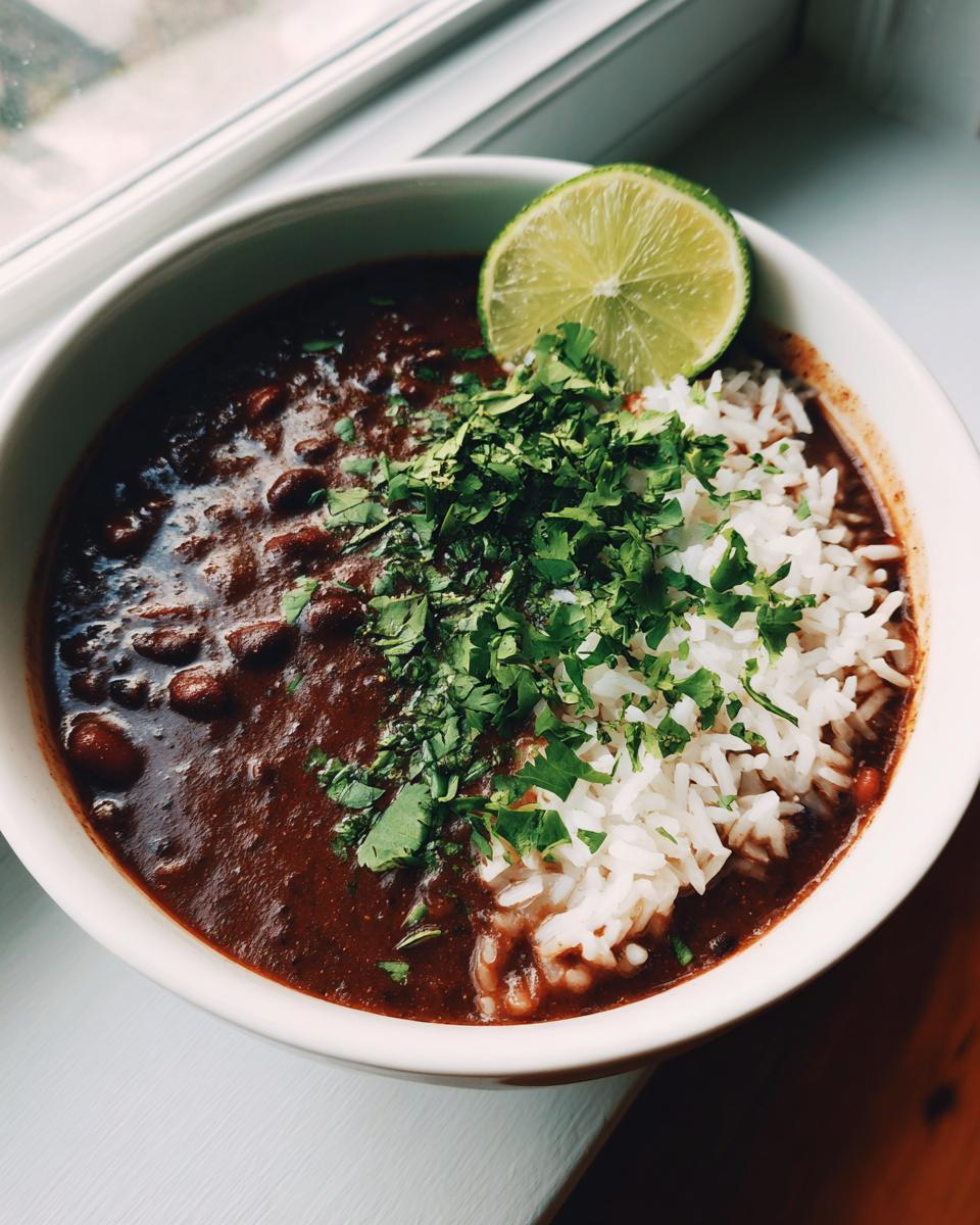 A bowl of rich black bean and rice soup topped with fresh cilantro and a lime wedge.