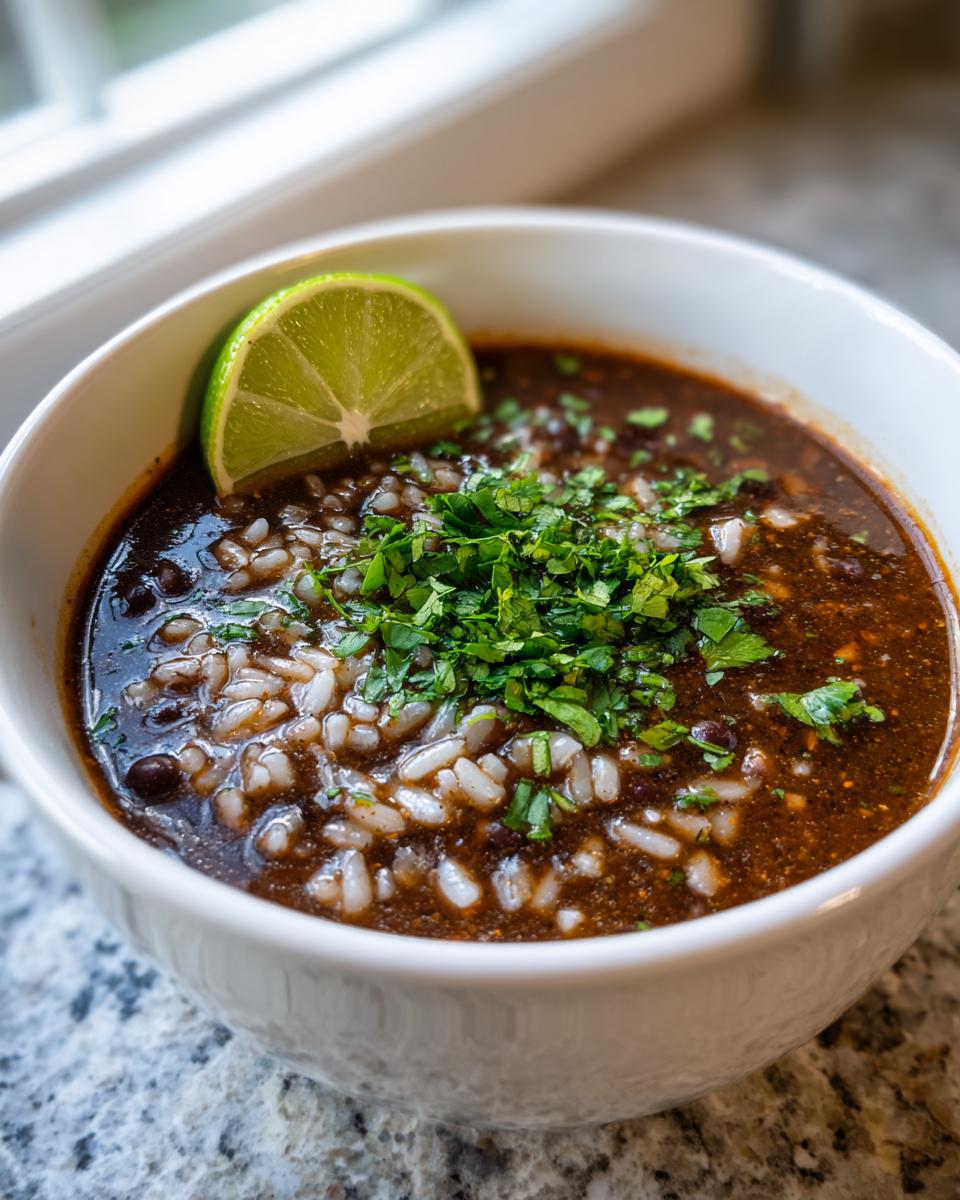 A close-up of rich black bean and rice soup topped with fresh cilantro and a lime wedge.