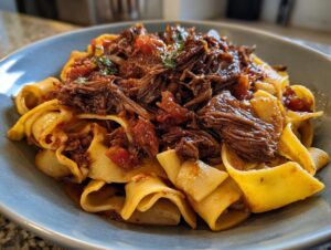 Close-up of rich, tender braised short rib pasta featuring wide pappardelle noodles and a deep red sauce.