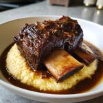 Close-up of tender braised short ribs dutch oven served over creamy yellow polenta with rich brown sauce.