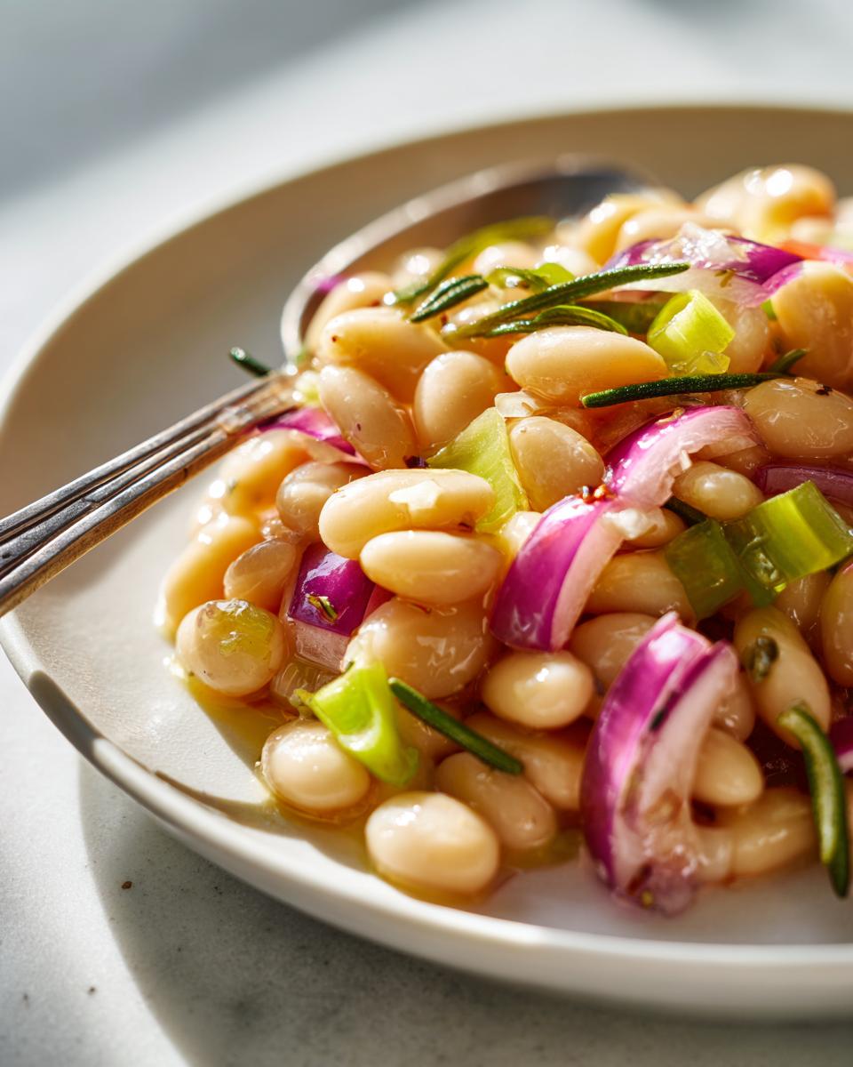 Close-up of a serving of vibrant white bean salad featuring cannellini beans, sliced red onion, green celery, and rosemary.