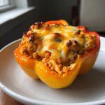 A baked yellow buffalo chicken stuffed pepper overflowing with cheesy ground chicken filling.