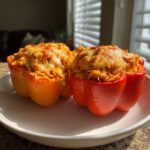 Two vibrant buffalo chicken stuffed peppers, one red and one orange, topped with melted, slightly browned cheese.