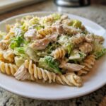 A close-up of a serving of caesar chicken pasta salad featuring rotini pasta, shredded chicken, and romaine lettuce.