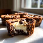 Close-up of a chocolate chip cheesecake cookie cup with a bite taken out, revealing creamy white cheesecake filling.