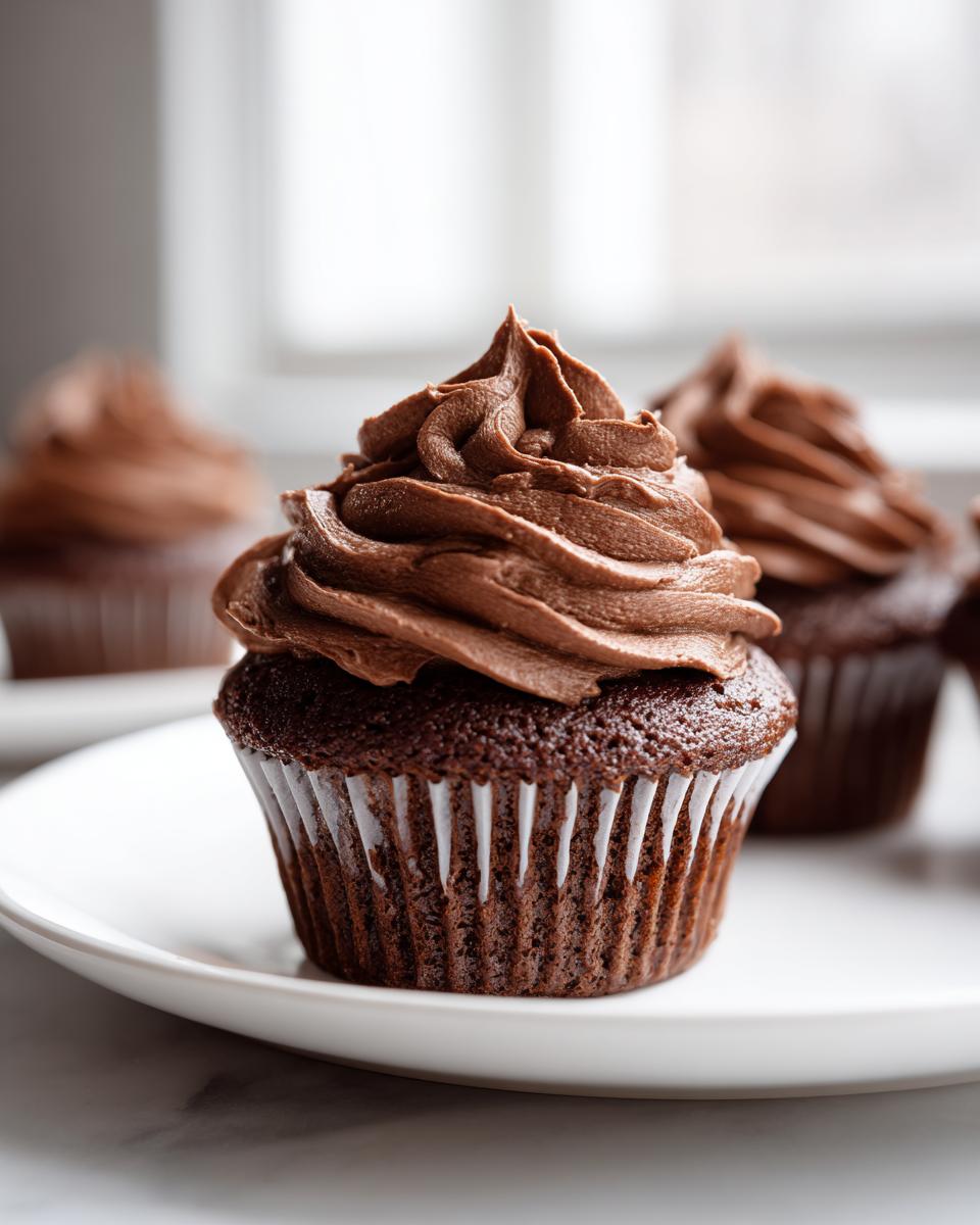 A close-up of a chocolate cupcake topped high with perfectly piped whipped chocolate buttercream frosting.