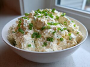 A white bowl filled with creamy cold crab dip, garnished generously with fresh chopped green chives.