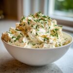 A white bowl filled with creamy, textured cold crab dip, generously garnished with fresh green chives.