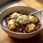 Close-up of a bowl filled with rich, creamy ground beef and dumplings, garnished with fresh thyme.