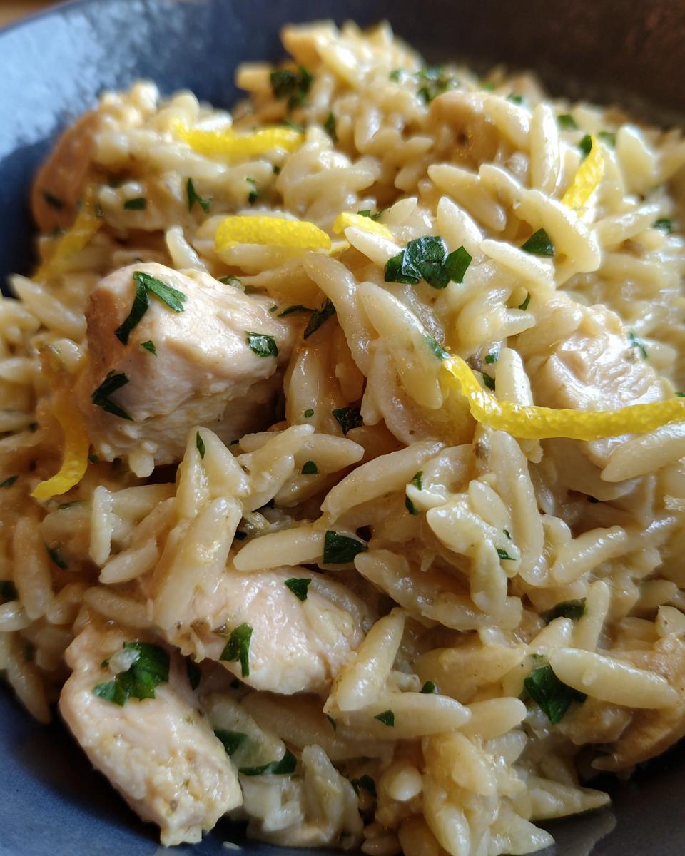 Close-up of creamy lemon chicken orzo pasta garnished with fresh parsley and bright yellow lemon zest.