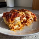 A close-up of a cheesy, saucy serving of crockpot ravioli lasagna on a white plate.
