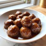 Close-up of tender meatballs coated in a thick, glossy swedish meatballs sauce in a white bowl.