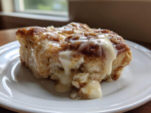 A close-up shot of a gooey, frosted slice of tiktok cinnamon roll casserole on a white plate.