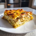 A thick slice of green chile chicken enchilada casserole with layers of shredded chicken and melted, browned cheese.