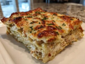 Close-up of a layered slice of green chile chicken enchilada casserole with melted, browned cheese topping.