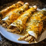 Close-up of three rolled green chile chicken enchiladas smothered in melted cheese on a white plate.