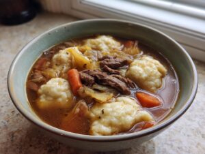 Close-up of a steaming bowl of ground beef and dumpling soup with carrots and rich broth.