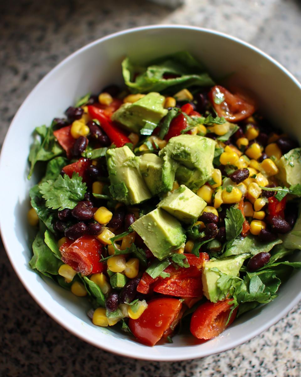 A vibrant bowl of healthy southwest salad featuring black beans, corn, tomatoes, and cubed avocado.