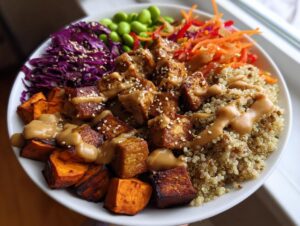 A vibrant, colorful buddha bowl featuring crispy tofu, roasted sweet potatoes, quinoa, and peanut sauce.