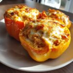 Three baked buffalo chicken stuffed peppers topped with melted, browned cheese served on a light plate.
