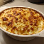 Close-up of hot baked crab dip in a white oval dish, featuring a bubbly, golden-brown melted cheese crust.