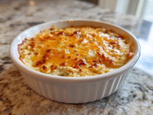 Close-up of a hot, baked crab dip recipe topped with melted, browned cheddar cheese in a white ramekin.