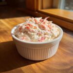 A small white ramekin filled with creamy imation crab dip recipe, highlighted by sunlight.