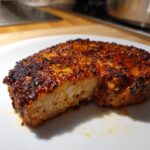 Close-up of a thick, juicy baked pork chop showing a rich, dark spice crust and moist interior.